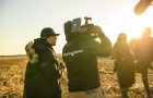 Four individuals centred around a video camera on location at sunset.