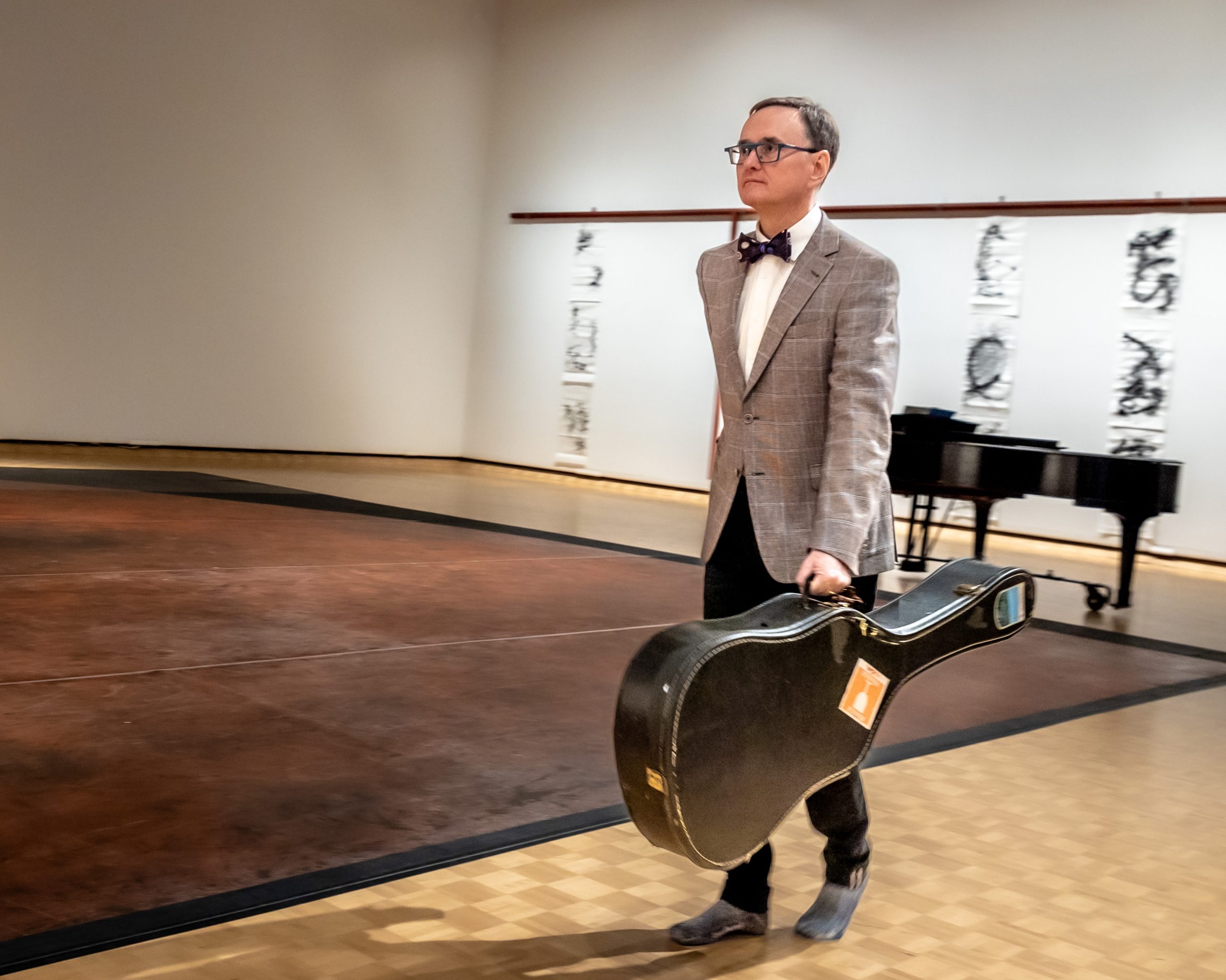 MAGdance2 Individual in art gallery walking with guitar case.