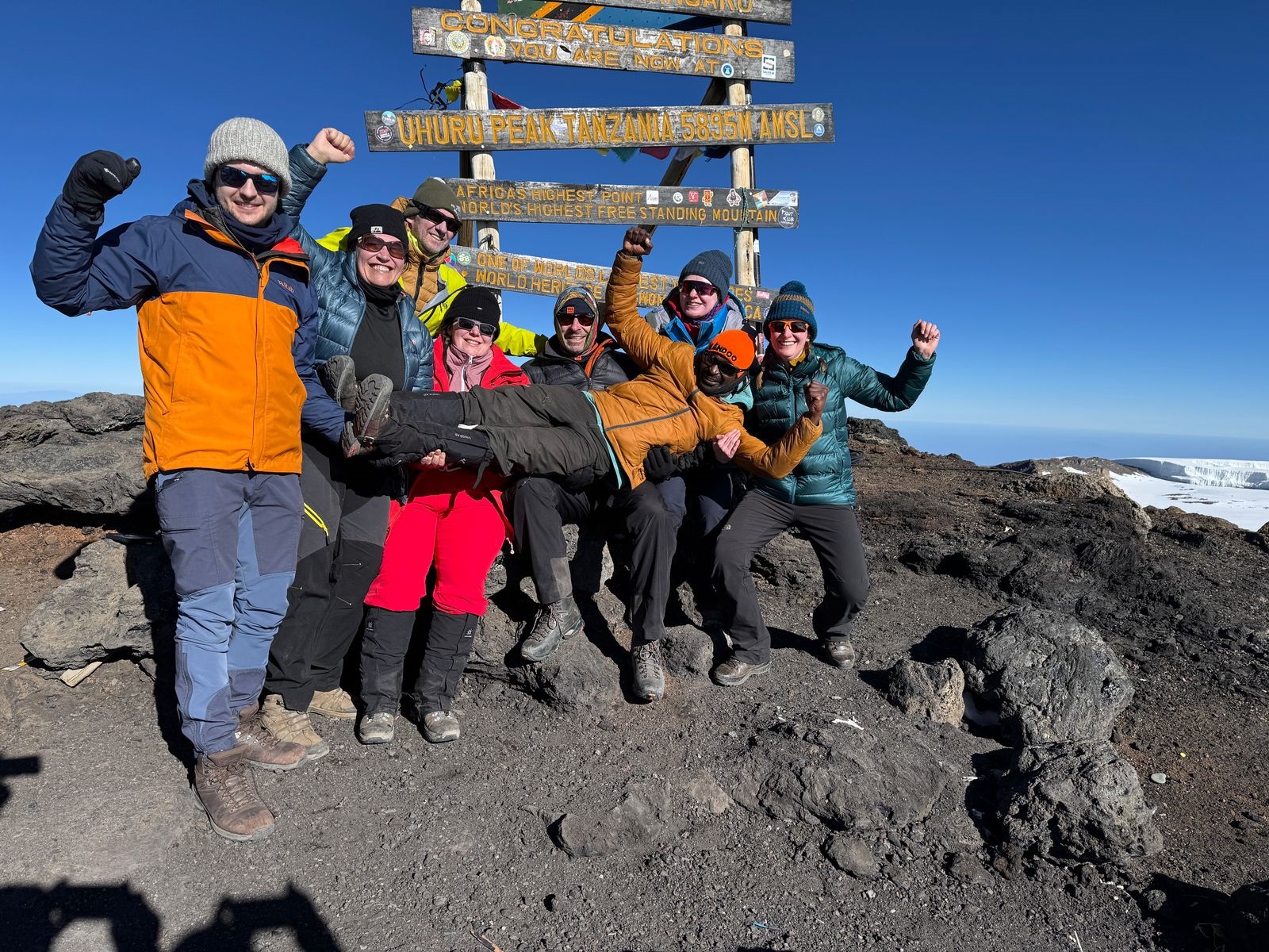 8e432eed-0902-4b19-a216-0b85e5ddaddb All seven members of InZania celebrate at Kilimanjaro's summit while Raymond, the group's lead guide, assumes a position of honour.